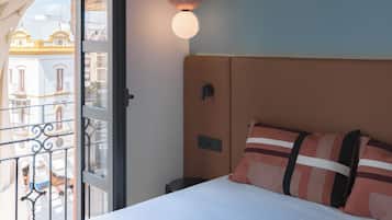 A hotel room with a bed, a hanging lamp, and a view of buildings through a window.