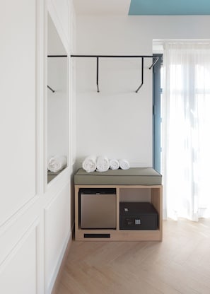 A room with a built-in wardrobe, a small seating area with towels, a compact dishwasher, and a window with sheer curtains. - Casa Candela Sevilla (Seville)