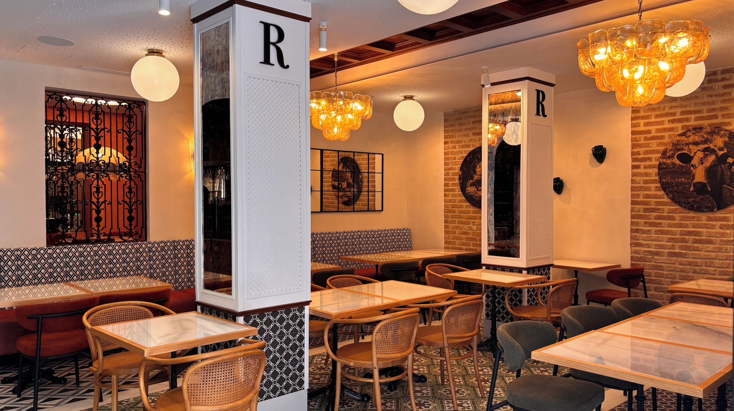 Un interior de restaurante con mesas y sillas de madera, una pared de ladrillo e iluminación decorativa.