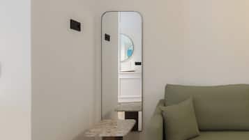Ein minimalistisches Wohnzimmer mit einem grünen Sofa, einem kleinen Holztisch und einem Spiegel an der Wand.