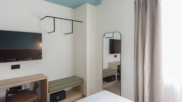 A hotel room with a bed, a desk, a chair, a TV mounted on the wall, and a mirror.