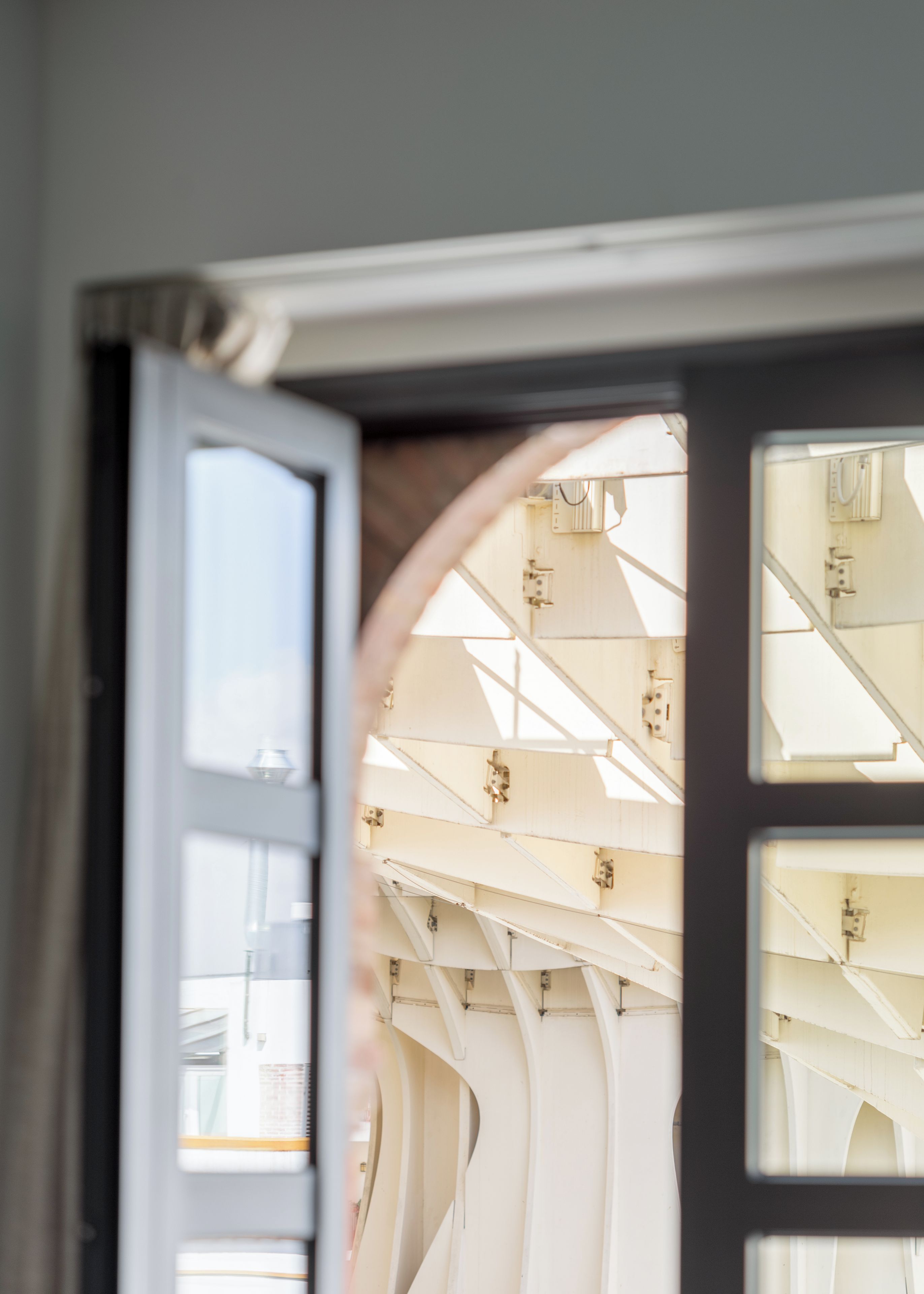 Puerta abierta que muestra el interior de una habitación, con una ventana y un techo con vigas estructurales.