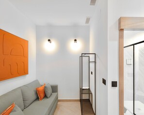 Una habitación de hotel moderna con un sofá gris, dos luces fijadas a la pared, una escalera de madera con marco y un suelo de baldosas.
