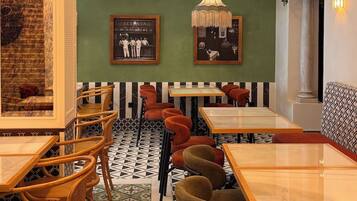 A restaurant interior with wooden tables and chairs, a patterned floor, a chandelier, and framed pictures on the wall.