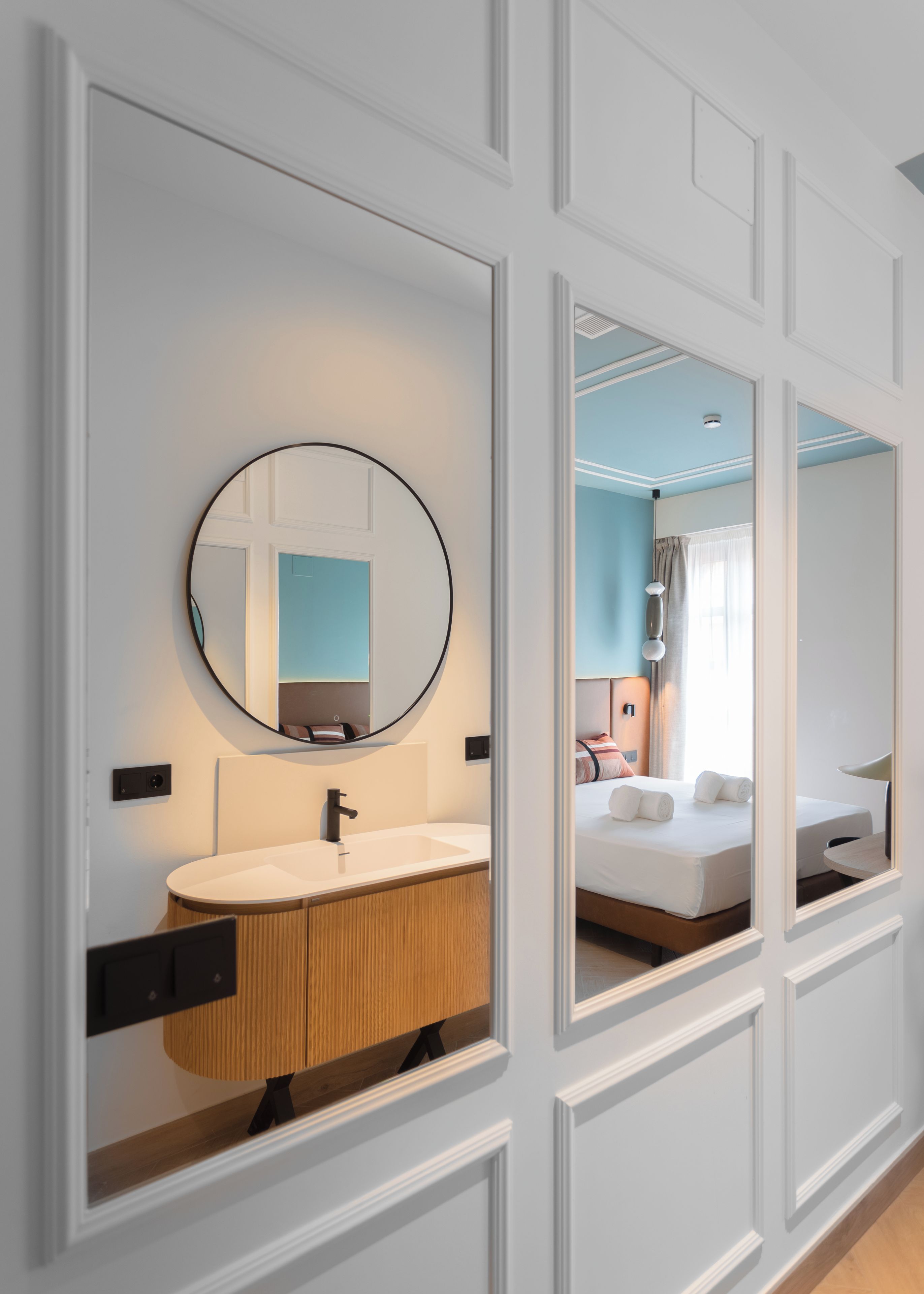 A modern bathroom with a round mirror, a white sink, and wooden cabinetry.