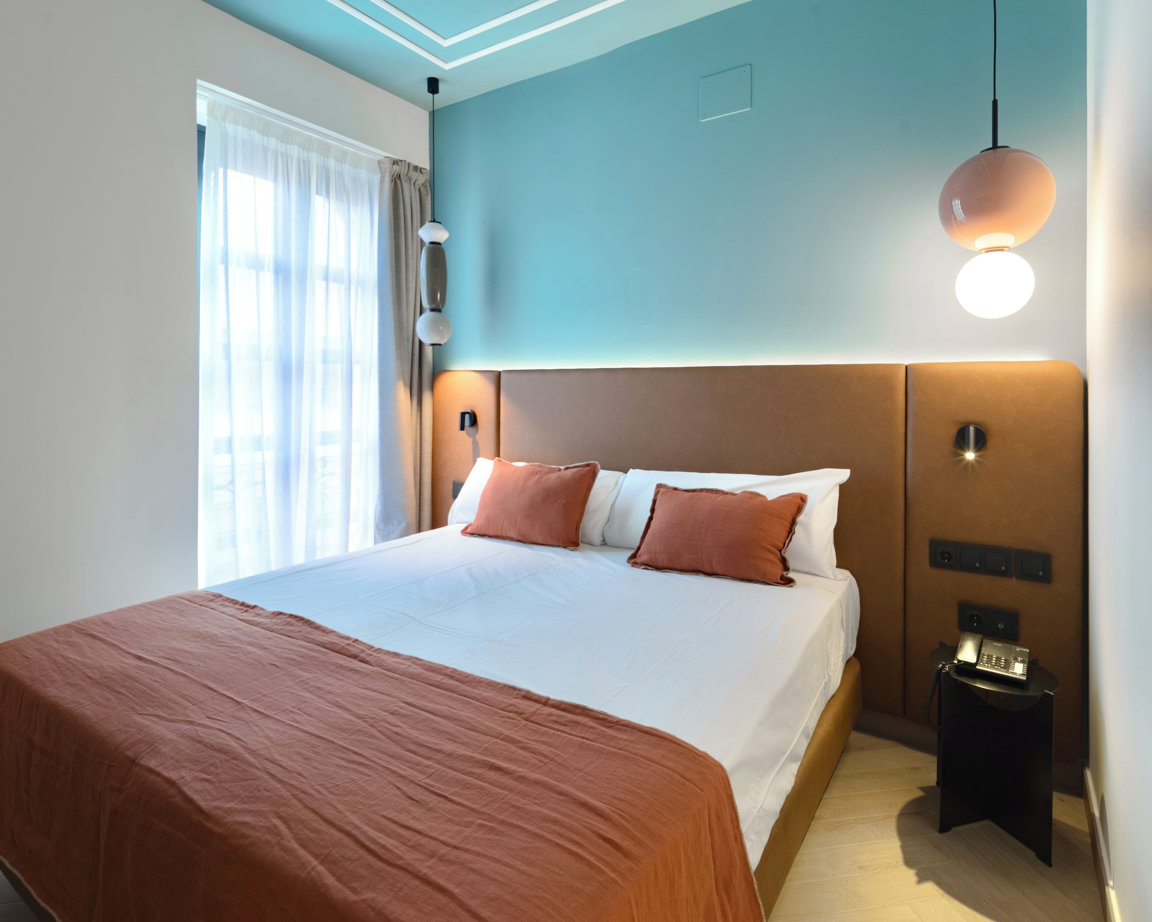 A hotel room with a large bed, a bedside table, a wall-mounted light, and a window with curtains.