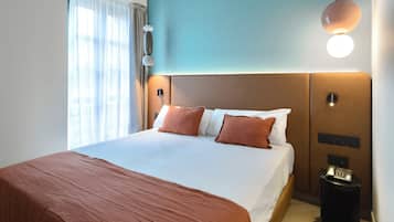 A hotel room with a large bed, a bedside table, a wall-mounted light, and a window with curtains.