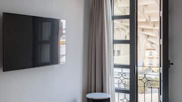 Une chambre d’hôtel avec un lit, un téléviseur fixé au mur, une petite table et un balcon donnant sur des immeubles.