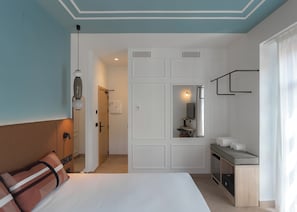 Une chambre d’hôtel comprenant un lit, un bureau avec un miroir, une petite kitchenette et une salle de bain visible à travers une porte ouverte.