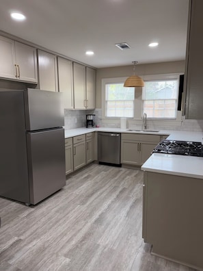 Una cocina moderna con refrigerador de acero inoxidable, lavavajillas, estufa a gas y una ventana con persianas.