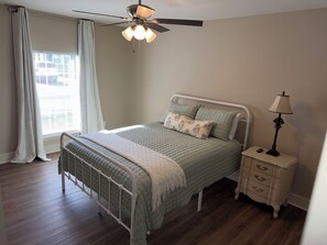 Ein Schlafzimmer mit einem Bett, einem Nachttisch, einer Lampe, einem Deckenventilator und einem Fenster mit Vorhängen.