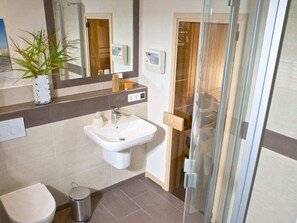 Ein modernes Badezimmer mit Waschbecken, Toilette, Mülleimer und einer Duschkabine aus Glas.