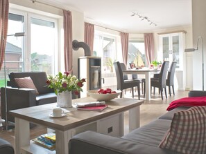 Ein modernes Wohnzimmer mit einer Couch, einem Couchtisch mit Büchern und einer Vase, einem Essbereich mit Tisch und Stühlen sowie einer Küche mit Schränken und einem Herd.
