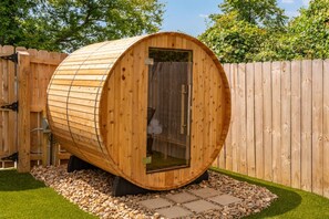 A wooden sauna with a curved roof, a glass door, and a surrounding gravel area. - Cowboy Cottage: Sleeps 12 (Nashville)