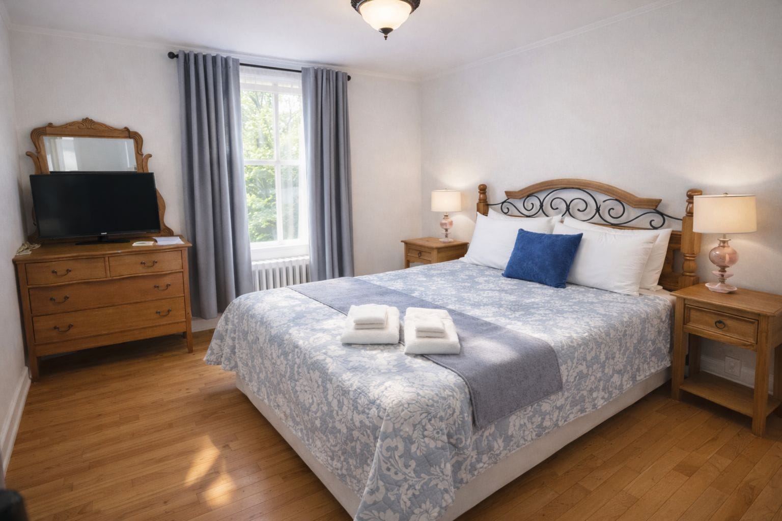 Une chambre à coucher comprenant un lit, une commode, un téléviseur et deux lampes de chevet.