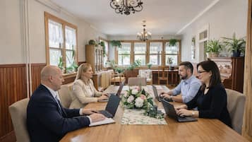 A conference room with a wooden table, four people seated, laptops, and a chandelier.