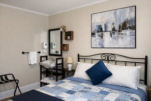 A bedroom with a bed, a nightstand, a mirror, a sink, and a wall-mounted painting. - Auberge Orpailleur chambre 201 (Val-d'Or)