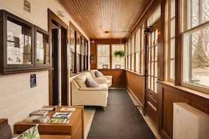 A corridor with a wooden ceiling, a beige sofa, and a table with magazines. - Auberge Orpailleur chambre 302 (Val-d'Or)