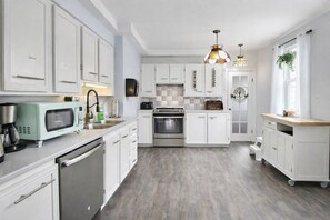 A modern kitchen with white cabinetry, stainless steel appliances, and a wooden countertop.