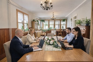 A conference room with a wooden table, four people seated, laptops, and a chandelier. - Auberge Orpailleur chambre 301 (Val-d'Or)