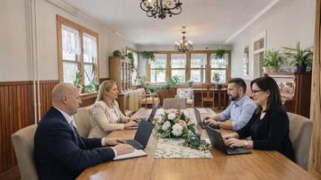 Une salle de conférence avec une table en bois, quatre personnes assises, des ordinateurs portables et un lustre.