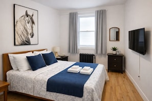 Une chambre à coucher avec un lit, une table de chevet, une lampe, une télévision, un miroir et une fenêtre avec des rideaux.