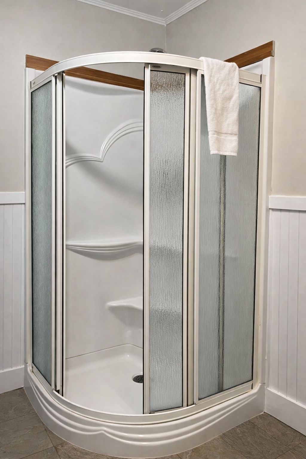 A corner shower with a glass door and a white towel hanging on the door.