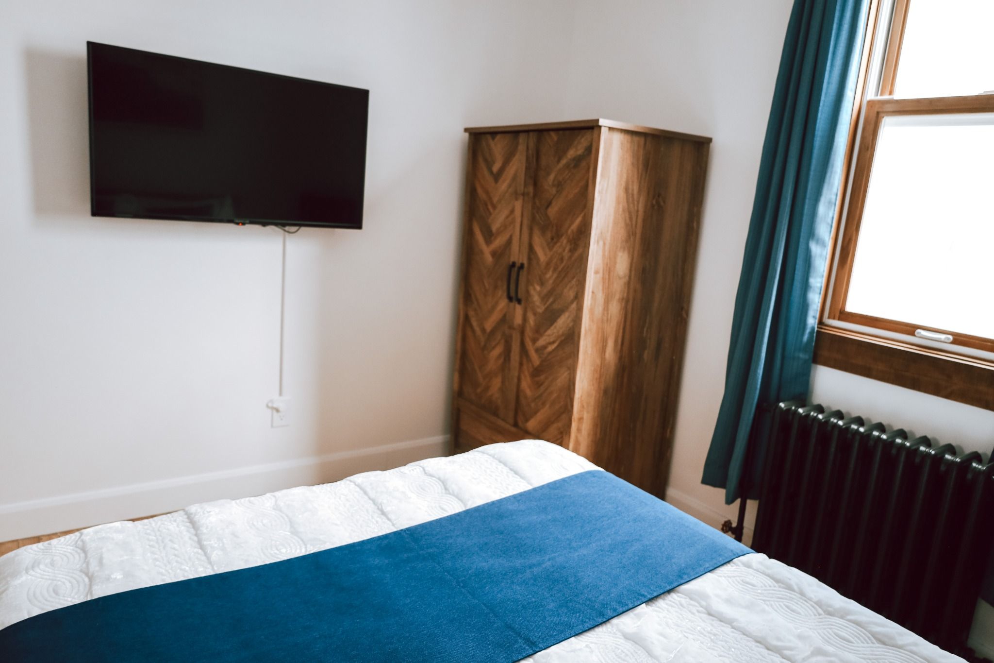A bedroom with a bed, a wardrobe, a television mounted on the wall, and a window with curtains.