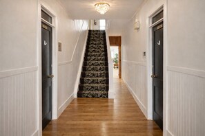 A hallway with a wooden floor, white wainscoting, and a staircase with patterned carpet. - Room 103 - private bathroom in a 1936 inn, Val-d'Or (Val-d'Or)