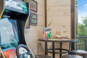 Eine Spielecke mit einer Rennspielmaschine, einem Brettspiel mit dem Titel 'SORRY!' und zwei Flaschen Corona Extra auf einem kleinen Tisch.