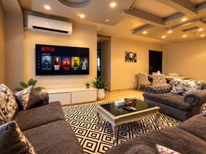 En moderne stue med et fladskærms-tv der viser Netflix, et sofabord, sofaer og et mønstret tæppe.