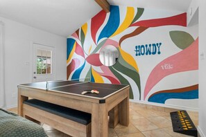 Ein Tischtennis-Tisch in einem Raum mit einem farbenfrohen, abstrakten Wandgemälde, in dessen Mitte das Wort 'HOWDY' steht.