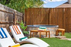 Un giardino sul retro con una vasca idromassaggio, poltrone relax e un tavolo di legno.