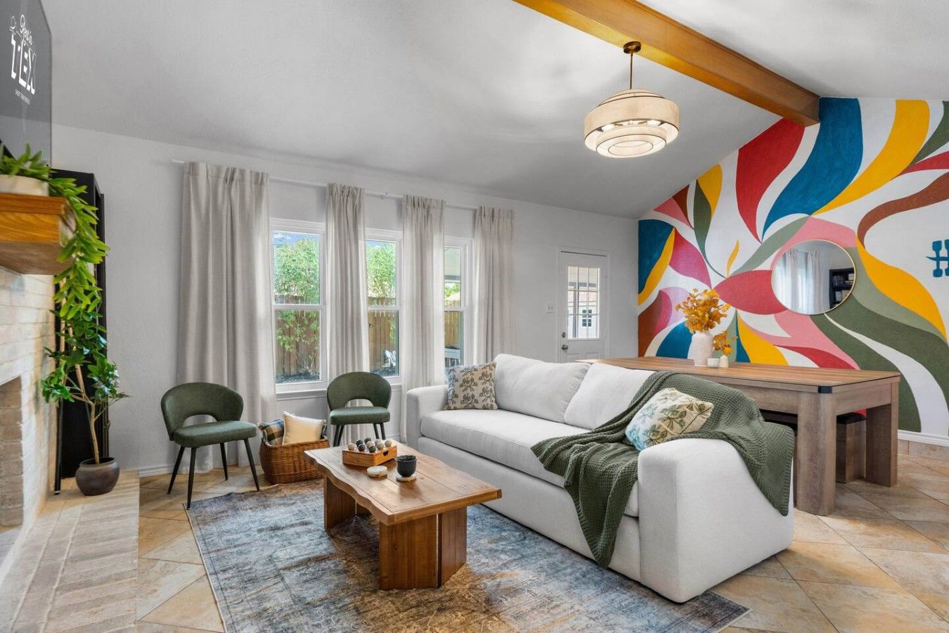 A modern living room with a white sofa, two green chairs, a wooden coffee table, and a colorful abstract wall mural.