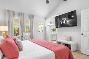 Una camera da letto con un letto, una TV a muro, una scrivania e una finestra con tende.