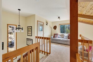 Una sala de estar con un sofá, una escalera de madera y vistas al exterior.