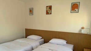 A hotel room with two single beds, a wooden headboard, a bedside table, and three wall-mounted artworks. - Lesiri hotel (Yang Si Surat)