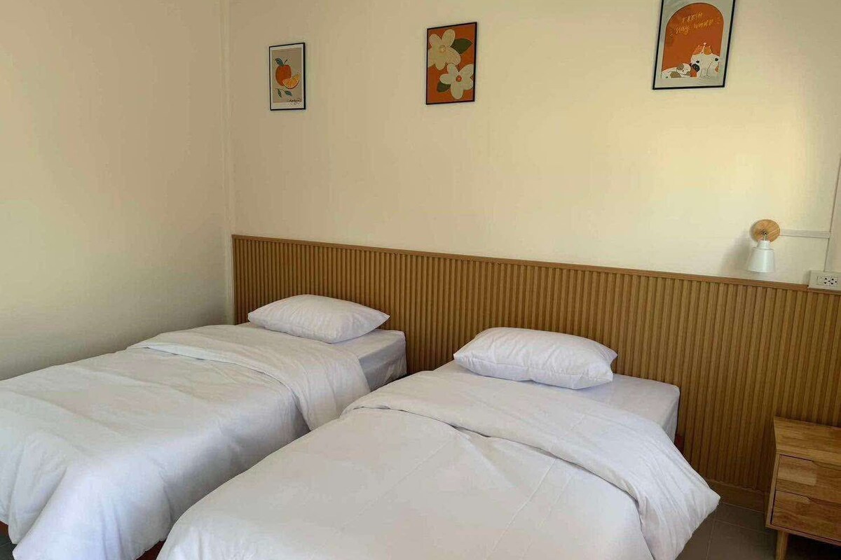 Une chambre d’hôtel avec deux lits simples, une tête de lit en bois, une table de chevet et trois œuvres d’art accrochées au mur.