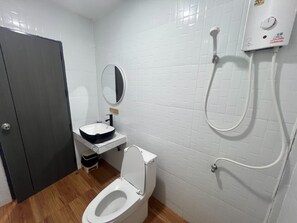 Une salle de bain avec des toilettes blanches, un lavabo avec un receveur noir, un miroir et une douche.