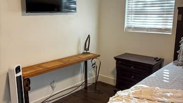 Un dormitorio con cama, televisor montado en la pared, ventana con persianas y un calefactor en el suelo.