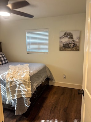 A bedroom with a bed, a window with blinds, a ceiling fan, and a wall-mounted picture. - Downtown Bryan Apt - Walk to Everything (Bryan)