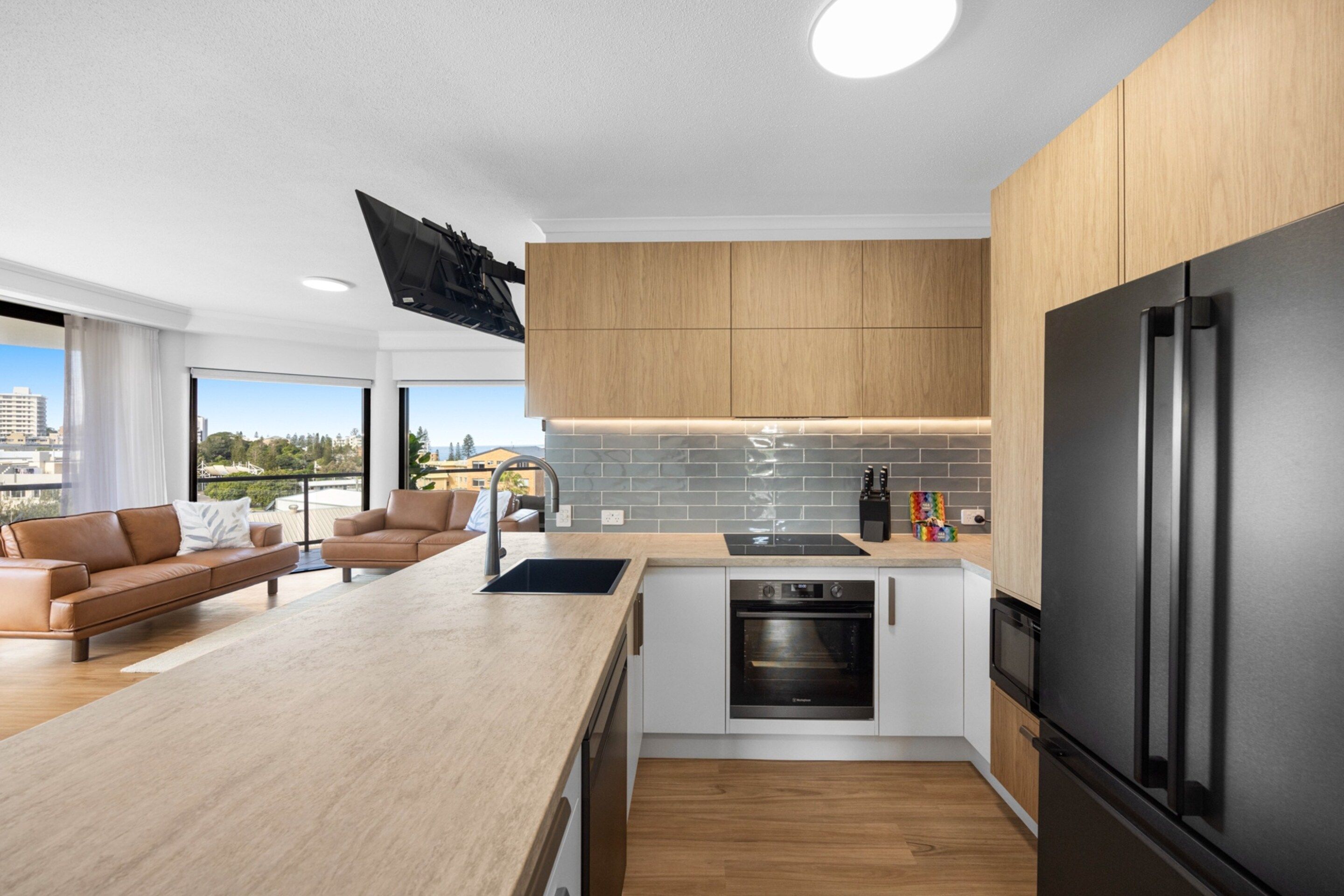 A modern kitchen with a built-in oven, a refrigerator, and a dining area with a sofa and a coffee table.