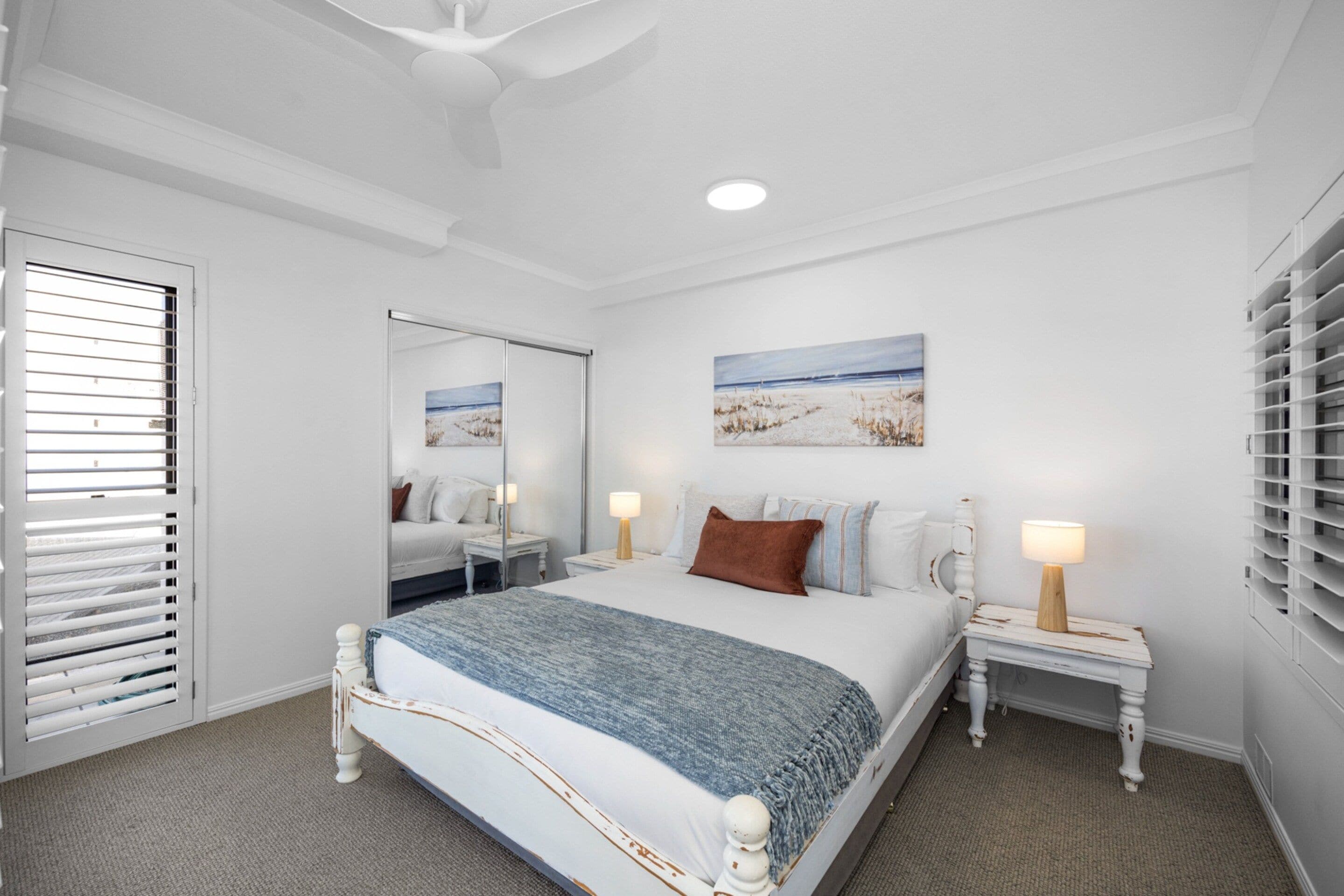 A bedroom with a bed, bedside tables, a mirror, and a painting on the wall.