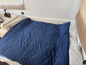 En säng med ett blått täcke, en vit kudde med ett geometriskt mönster och en beige sänggavel.