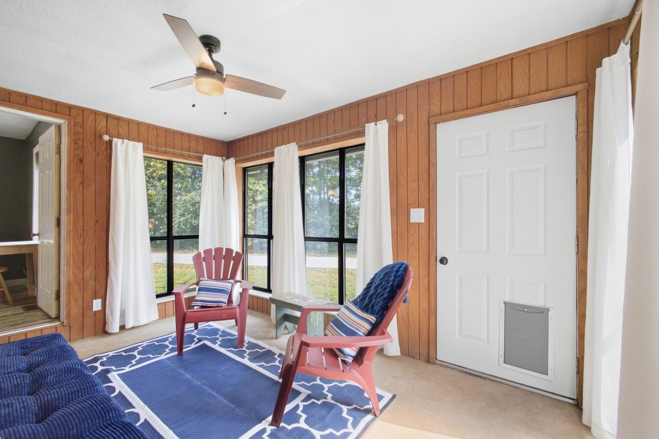 Une pièce dotée d’un ventilateur de plafond, de deux fauteuils Adirondack, d’une petite table et d’une porte avec un moustiquaire.