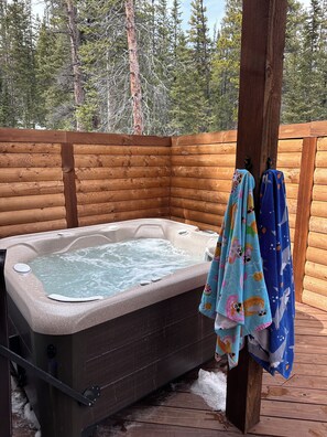 Een hottub met een houten terras en een omheining van hout in een bebost gebied.