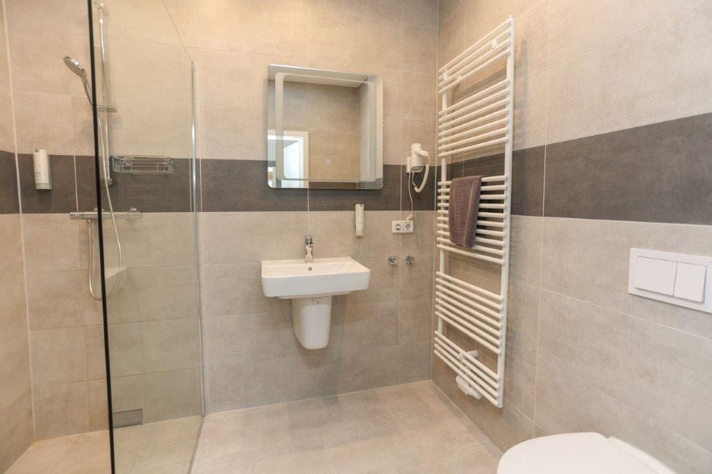 Ein modernes Badezimmer mit Duschkabine aus Glas, einem Standwaschbecken, einem Handtuchhalter und einem Spiegel.