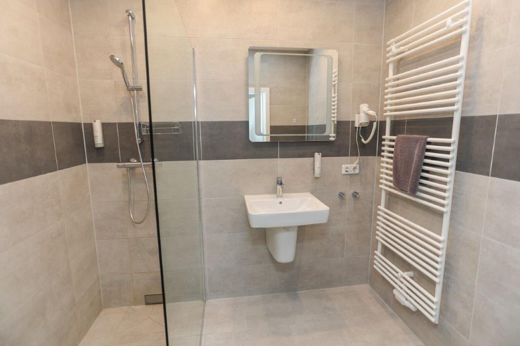 Un baño moderno con ducha de vidrio, un lavamanos blanco y un perchero para toallas.