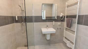 Un baño moderno con ducha de vidrio, un lavamanos blanco y un perchero para toallas.