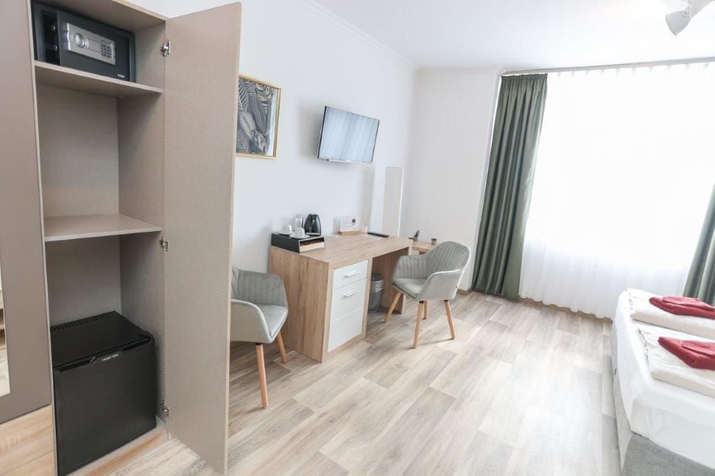 Ein Hotelzimmer mit Schreibtisch, zwei Stühlen, Fernseher, Kleiderschrank und einem Bett.